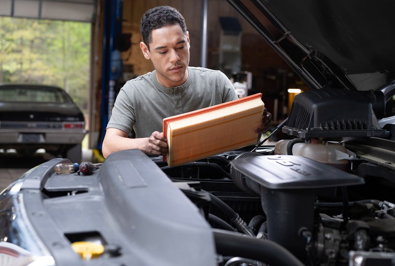 Person standing in front of a vehicle looking at an air filter