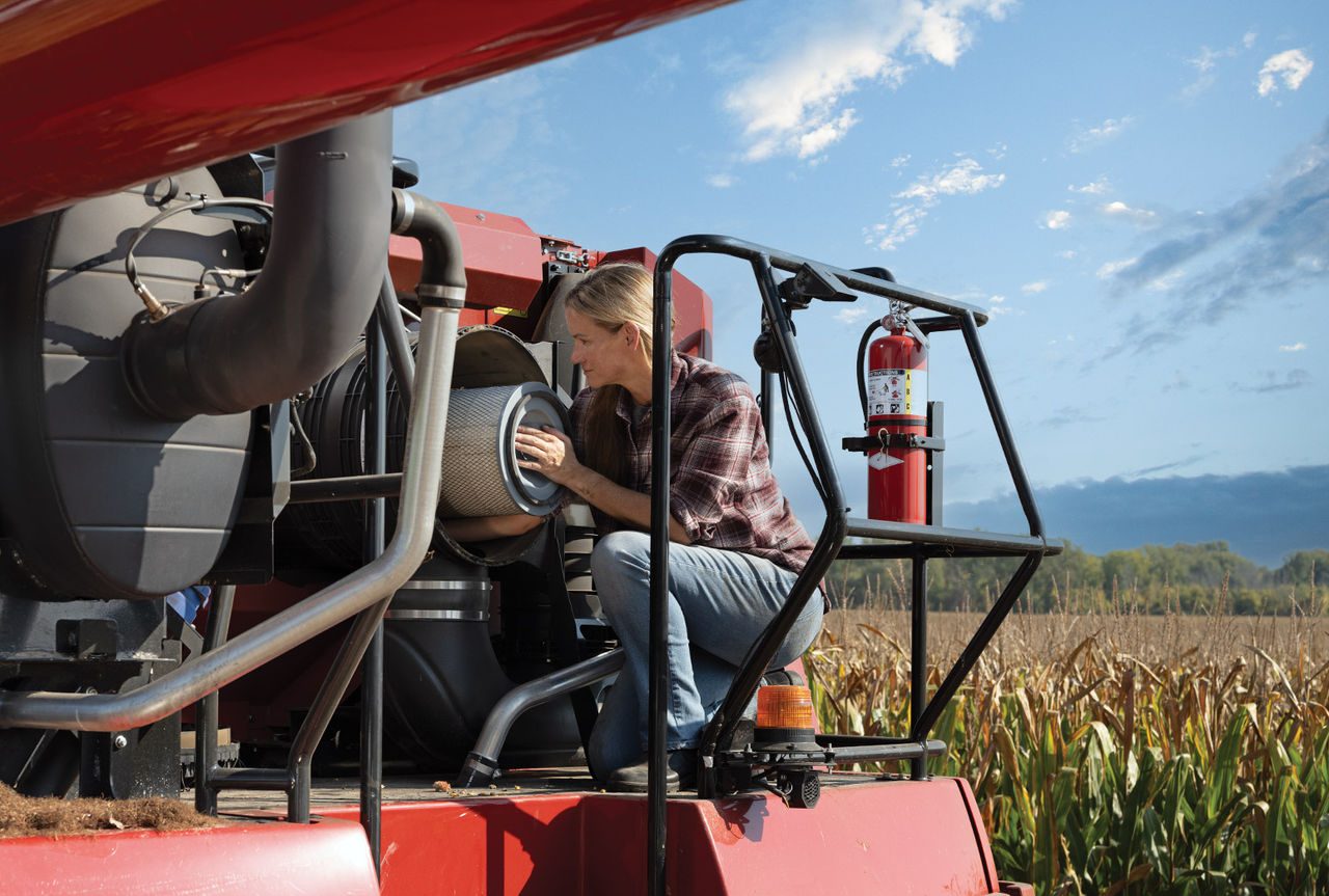 Woman changing a tractor's filter in a corn field